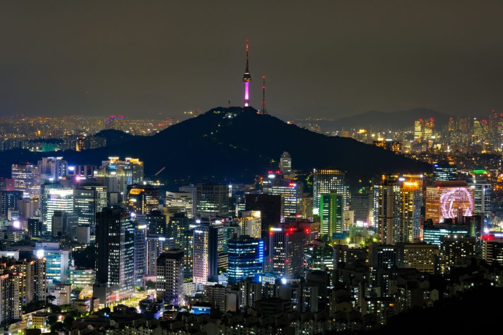 Seoul skyline at night with N Seoul Tower illuminated in purple above Namsan and brightly lit buildings in the foreground.